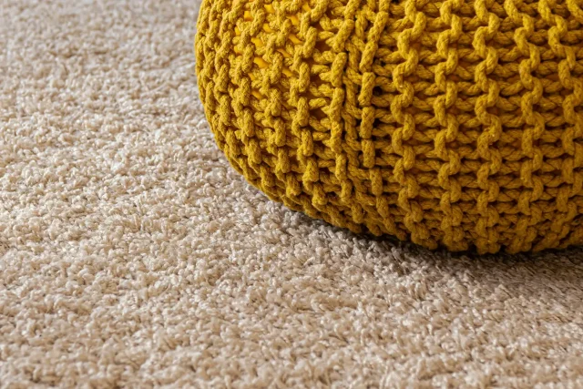 Close-up of thick beige cut pile carpet with a mustard yellow knitted pouf footstool